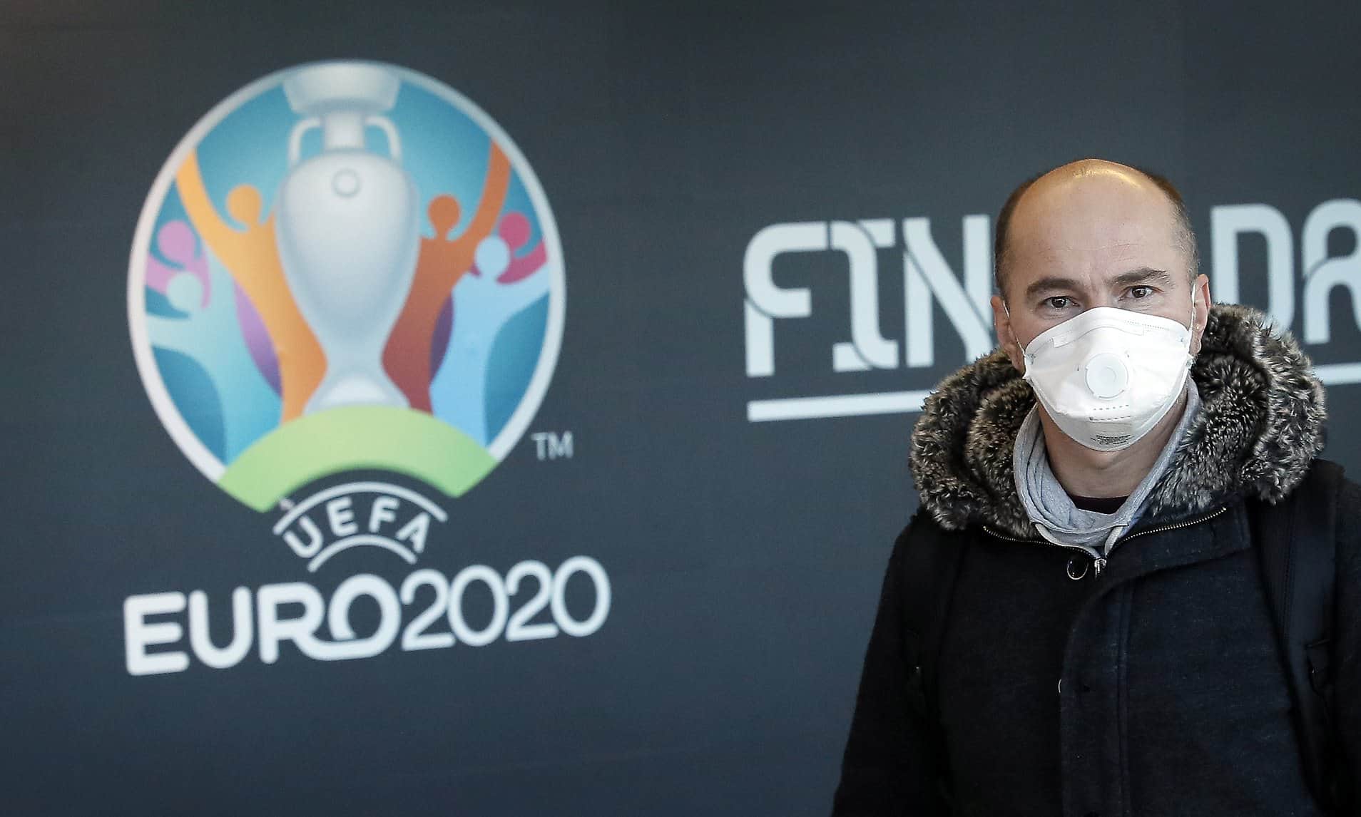COVID-19 mask on a face of a fan near the logo of canceled EURO 2020.